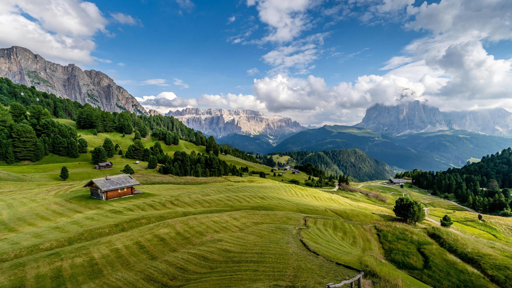 Scenic view of a mountainous landscape with a wooden cabin on a grassy hill.