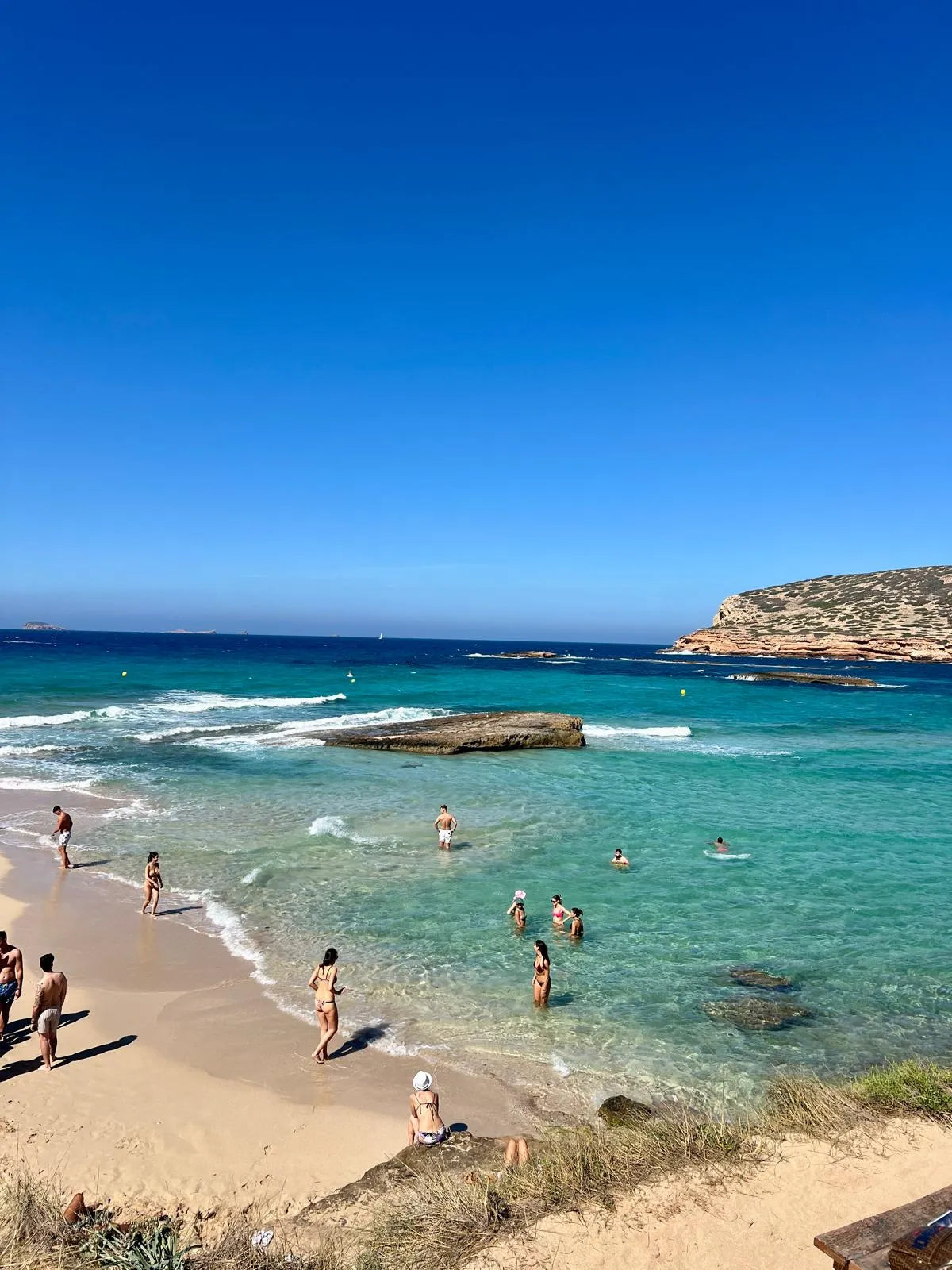 Beach scene with people swimming and sunbathing under a clear blue sky.