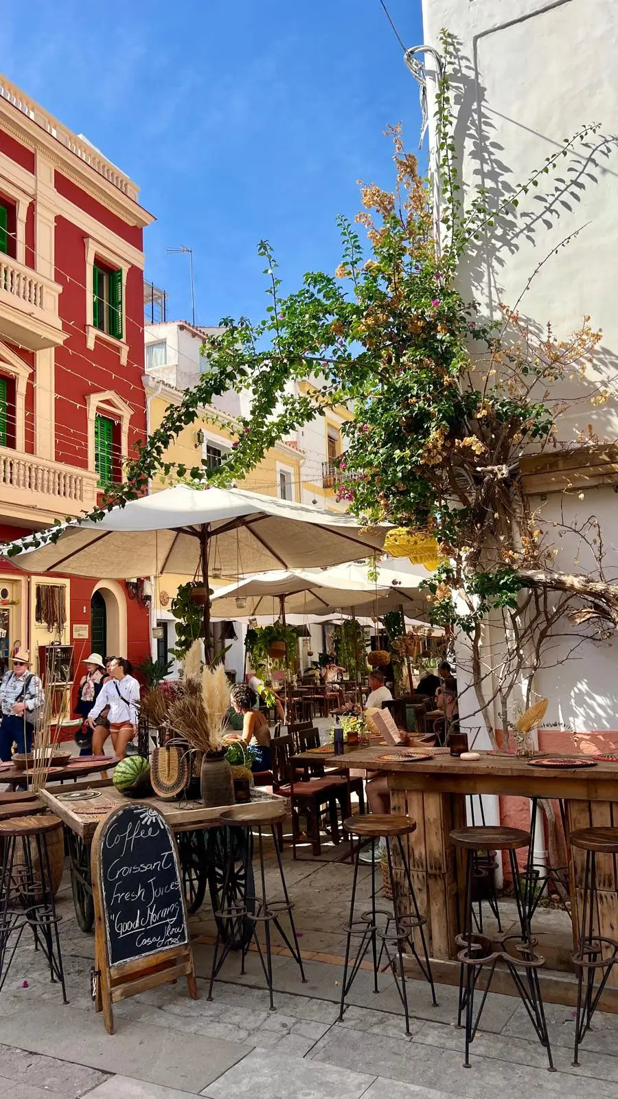 Outdoor cafe with tables, chairs, and umbrellas in a picturesque street setting.