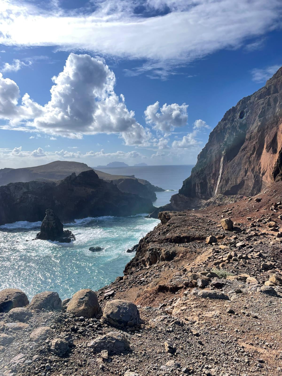 Scenic view of a coastal landscape with cliffs and ocean under a blue sky with clouds.