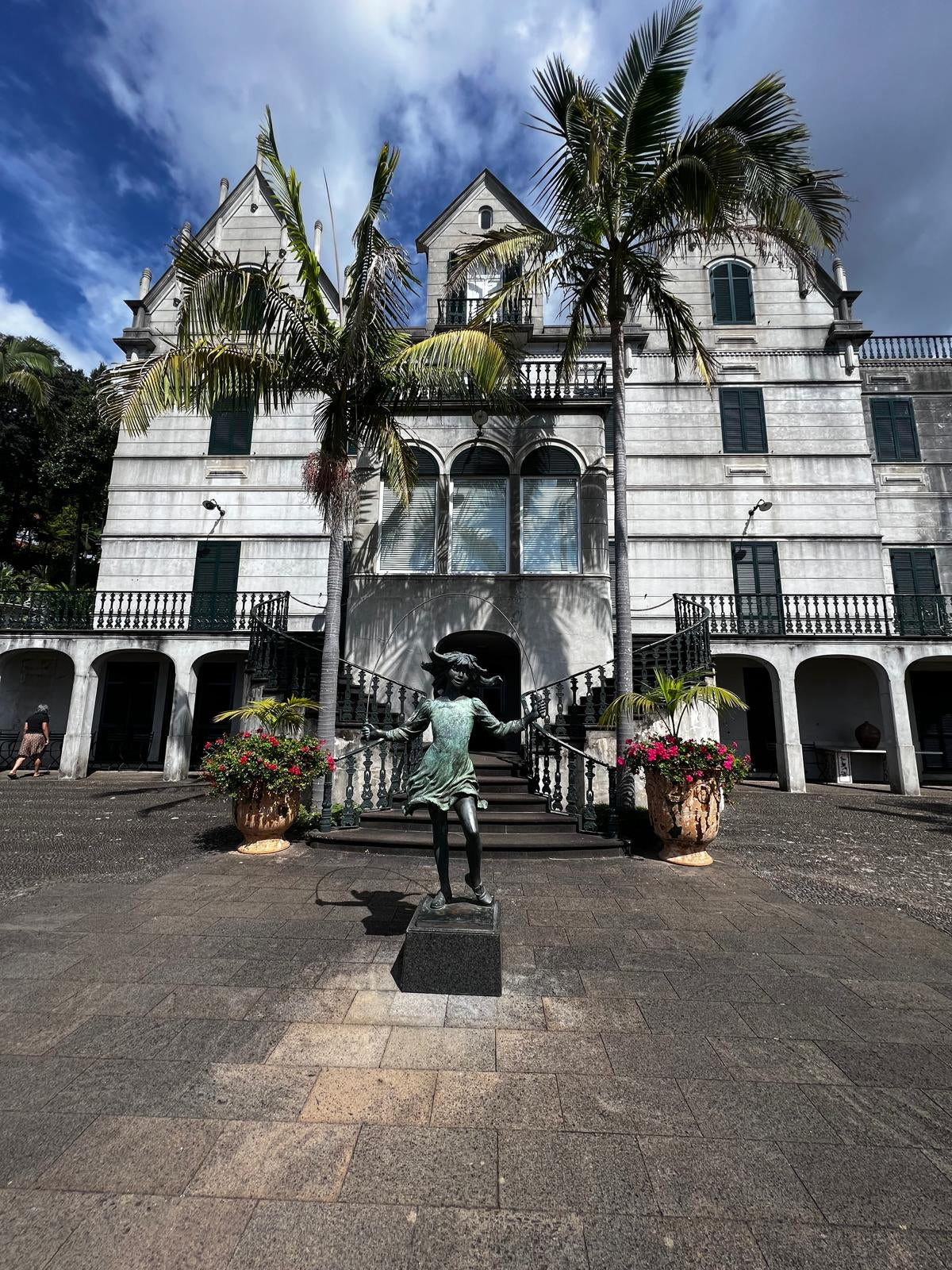Statue in front of a large white building with balconies and palm trees.