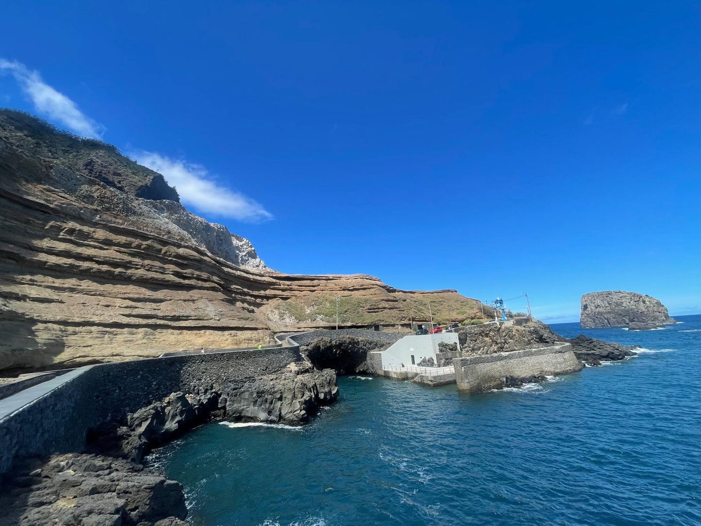 Coastal landscape with cliffs and a small building near the water under a clear blue sky.