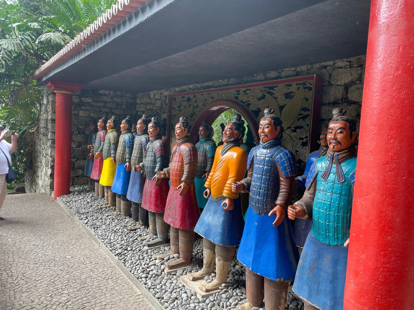 Row of statues in traditional attire along a path with a red column.