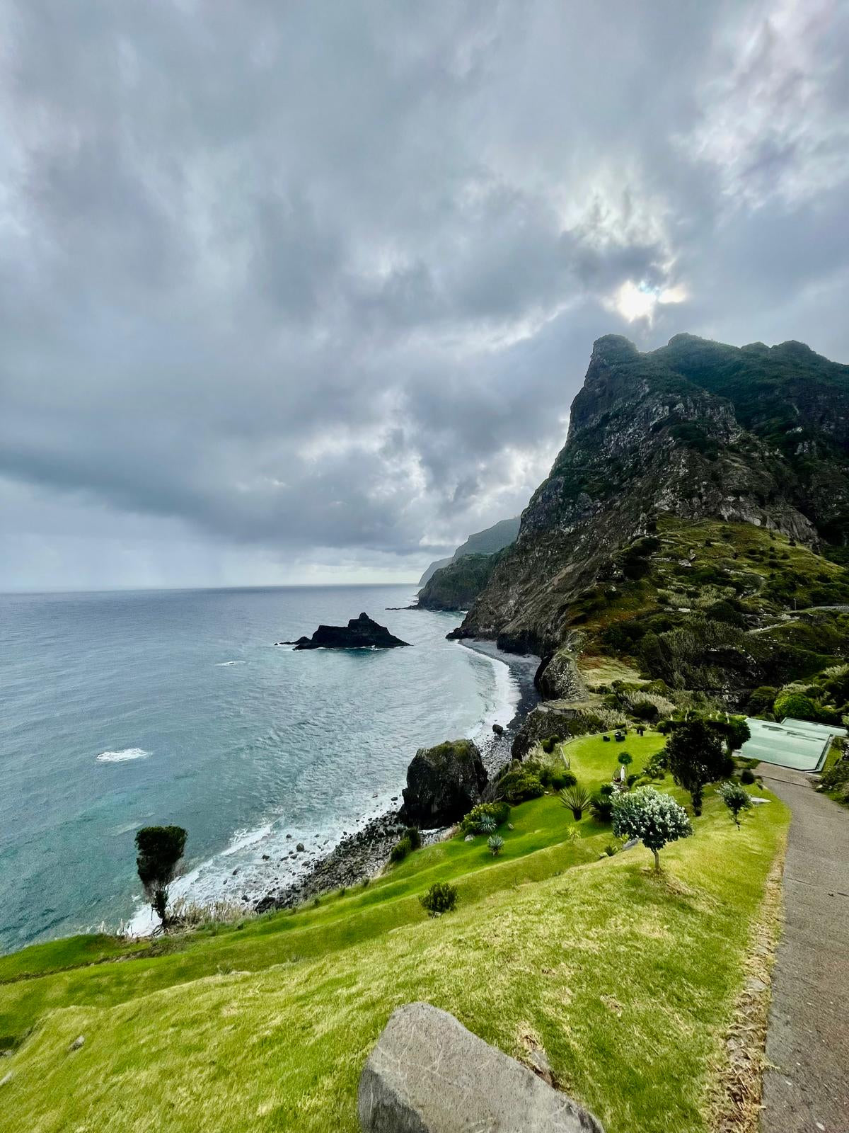 Coastal landscape with a path leading to a cliffside, under a cloudy sky.