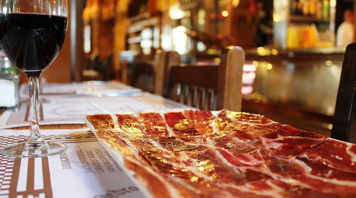 Platter of sliced cured meat next to a glass of red wine in a bar setting