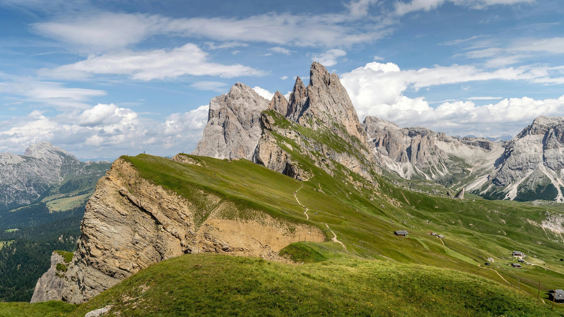 Mountain landscape with green grass and rocky peaks under a blue sky with clouds.