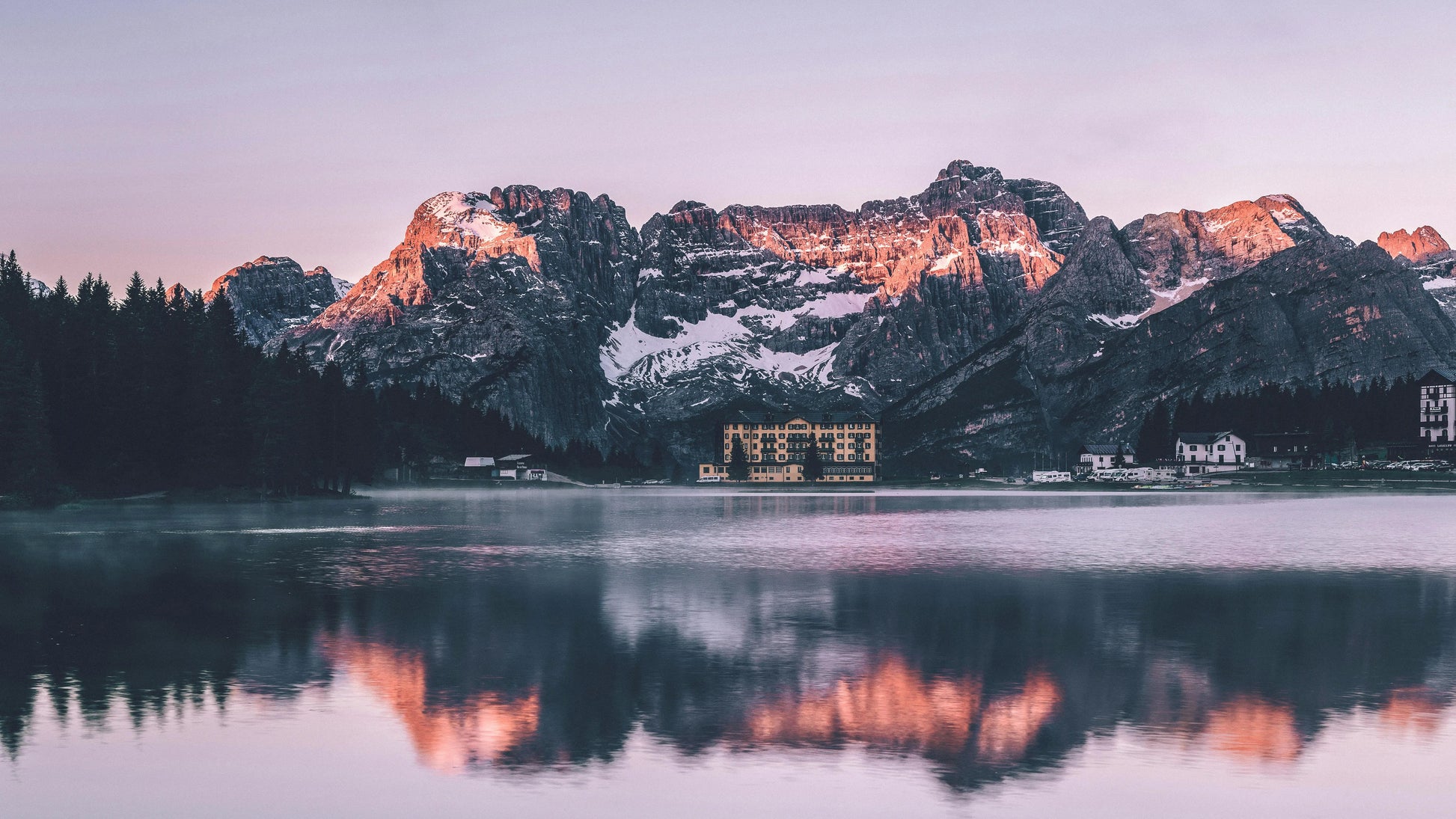 Mountain range with snow peaks reflected in a calm lake at dusk.