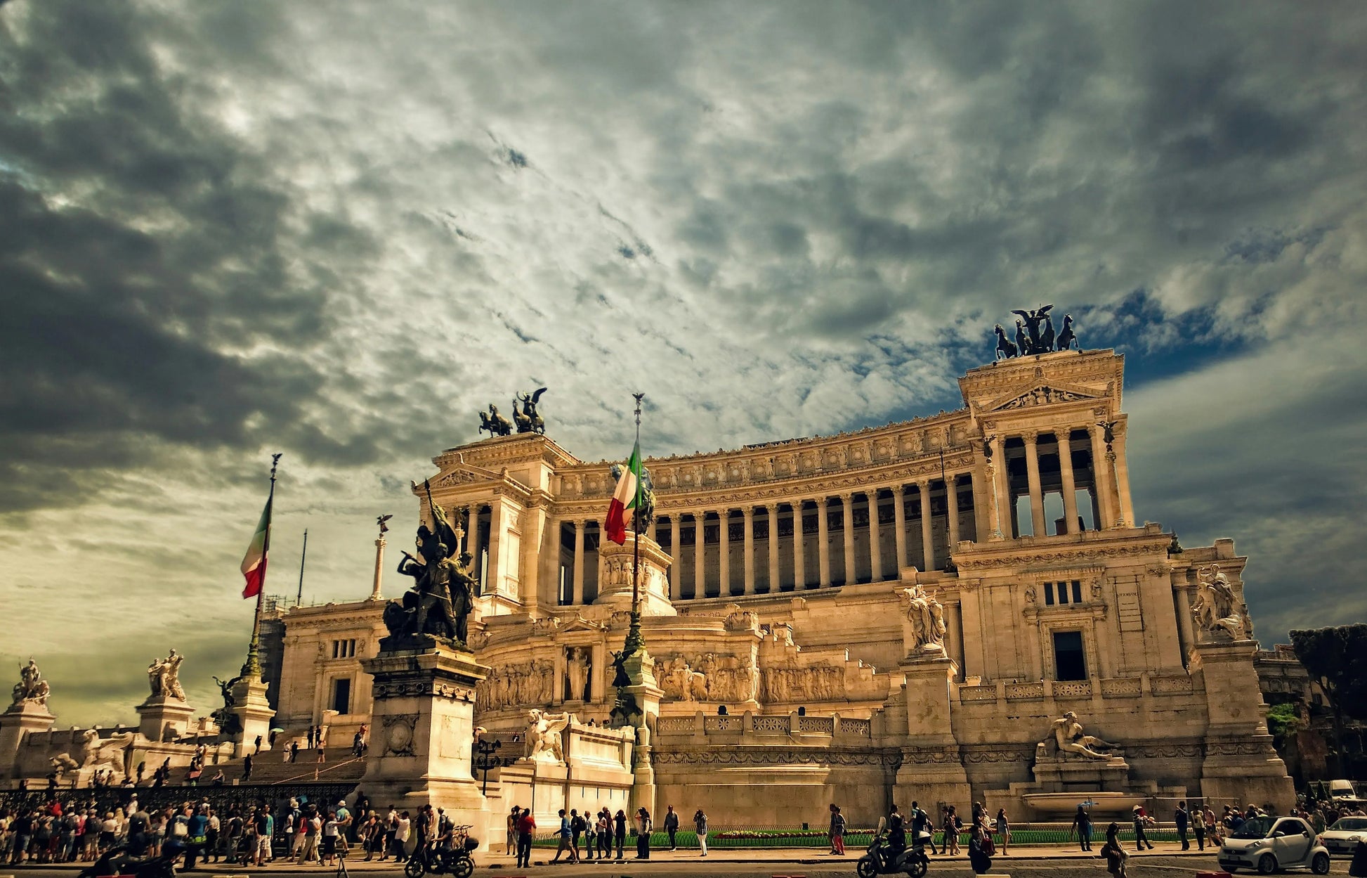 Large historical building with statues and flags under a cloudy sky