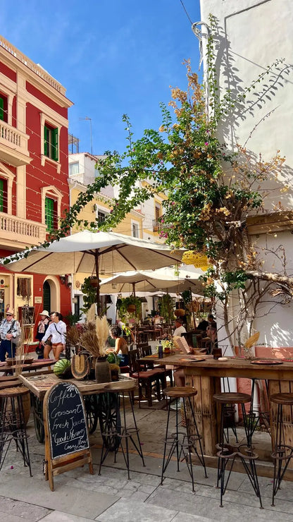 Outdoor cafe with tables, chairs, and umbrellas in a picturesque street setting.
