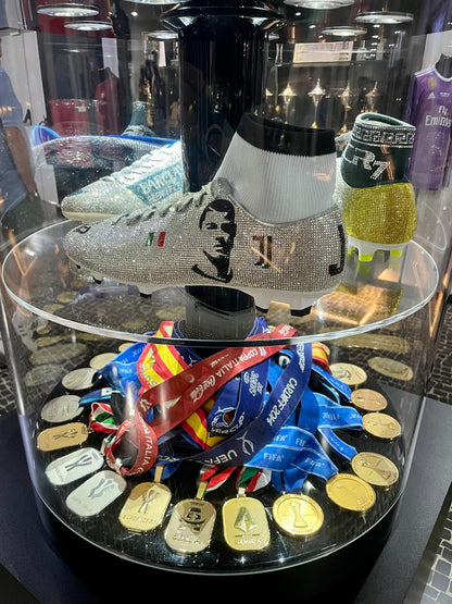 Shoe with rhinestone detailing on a glass display case with medals and ribbons.