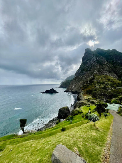 Coastal landscape with a path leading to a cliffside, under a cloudy sky.