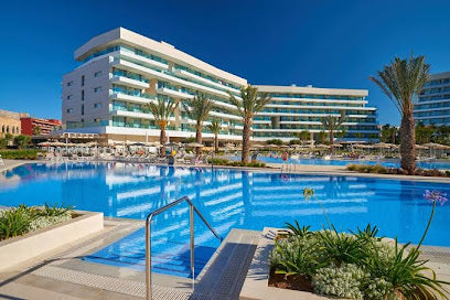 Hotel pool area with clear blue water, palm trees, and a modern building.