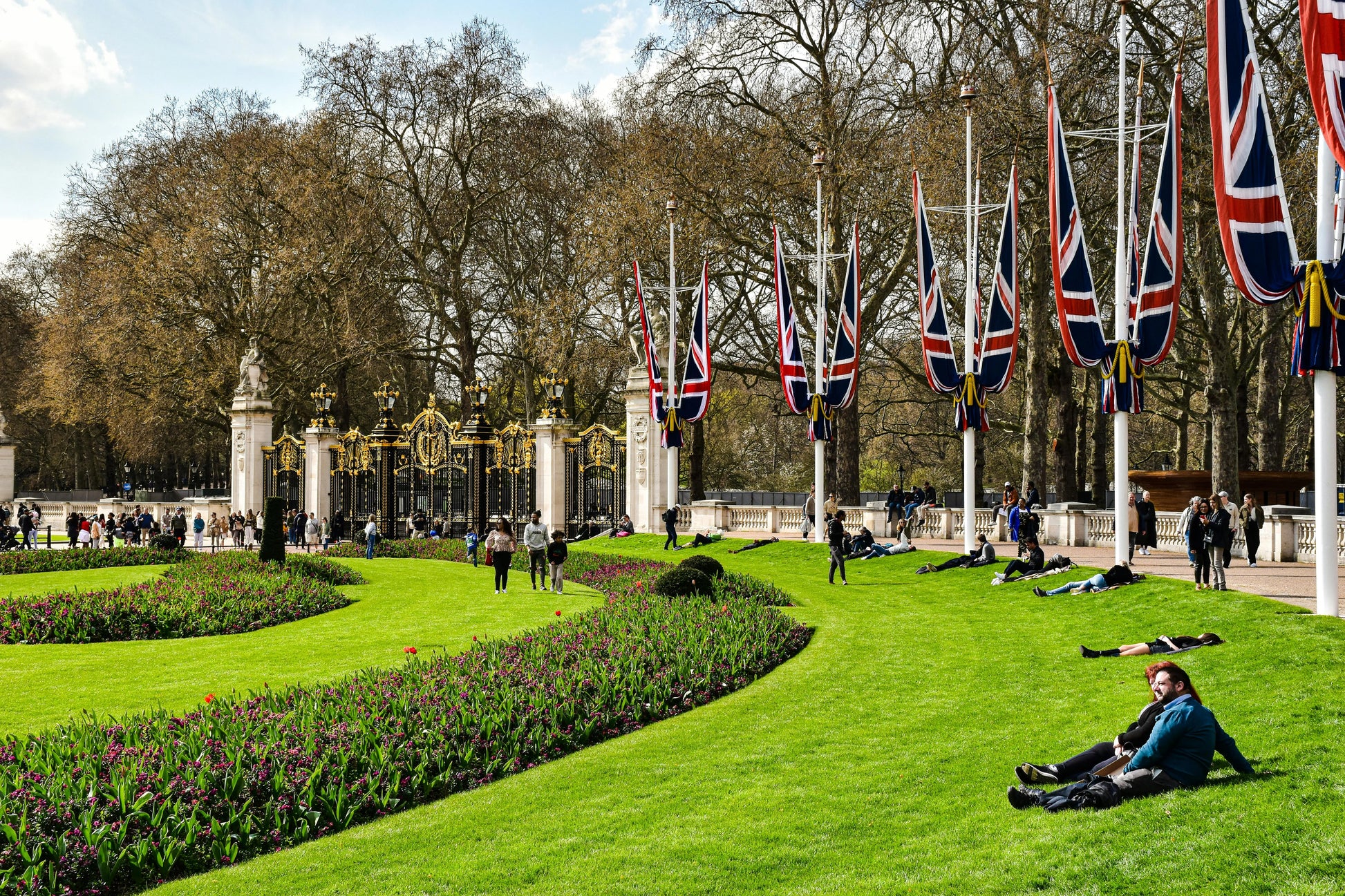Lush green park with people relaxing on the grass, featuring British flags in the background.