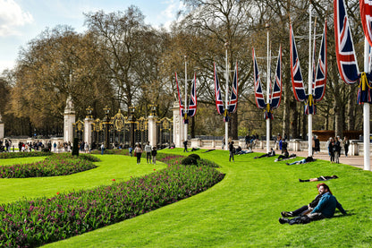 Lush green park with people relaxing on the grass, featuring British flags in the background.