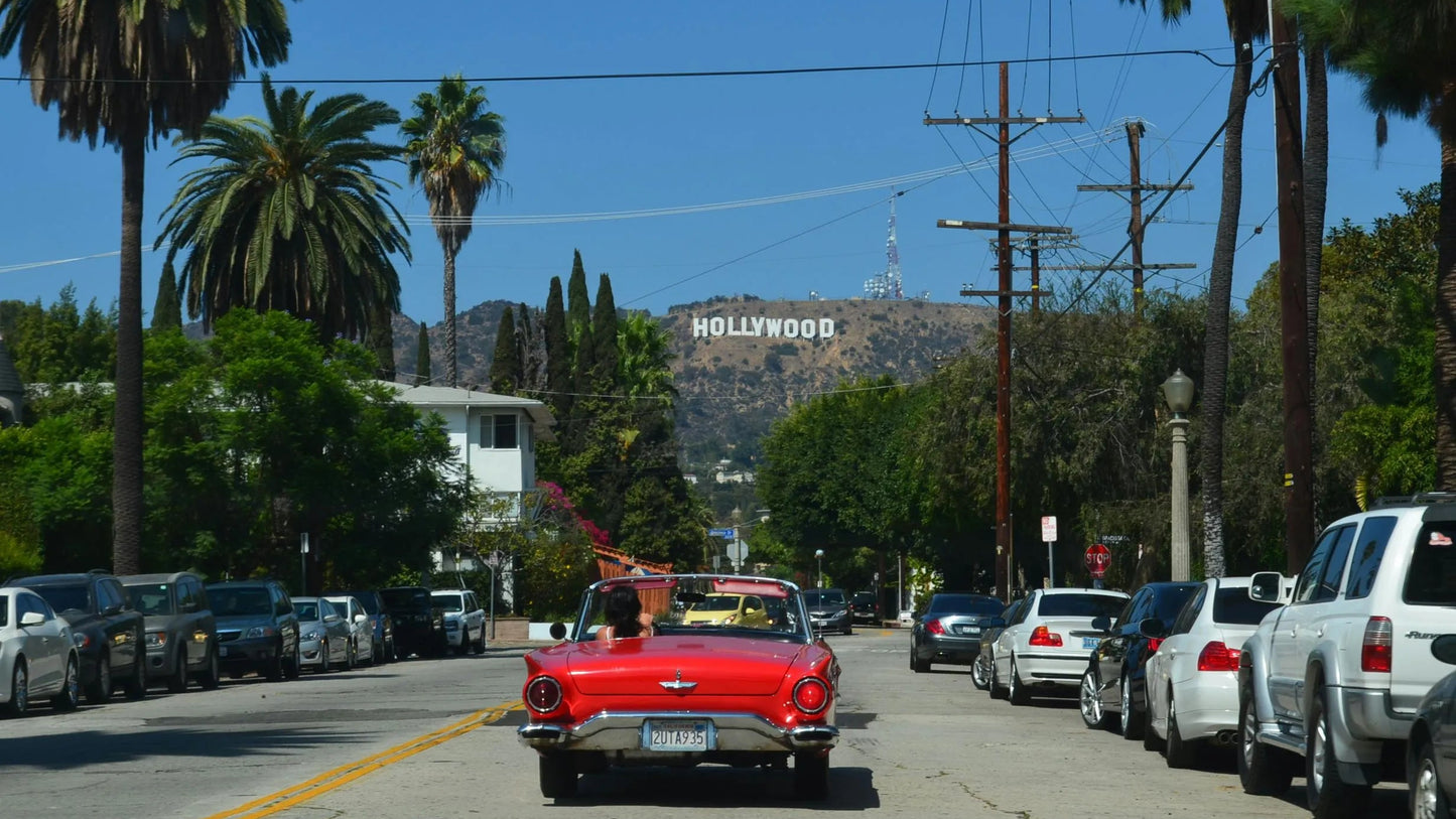 Red car on a street with palm trees and the Hollywood sign in the background