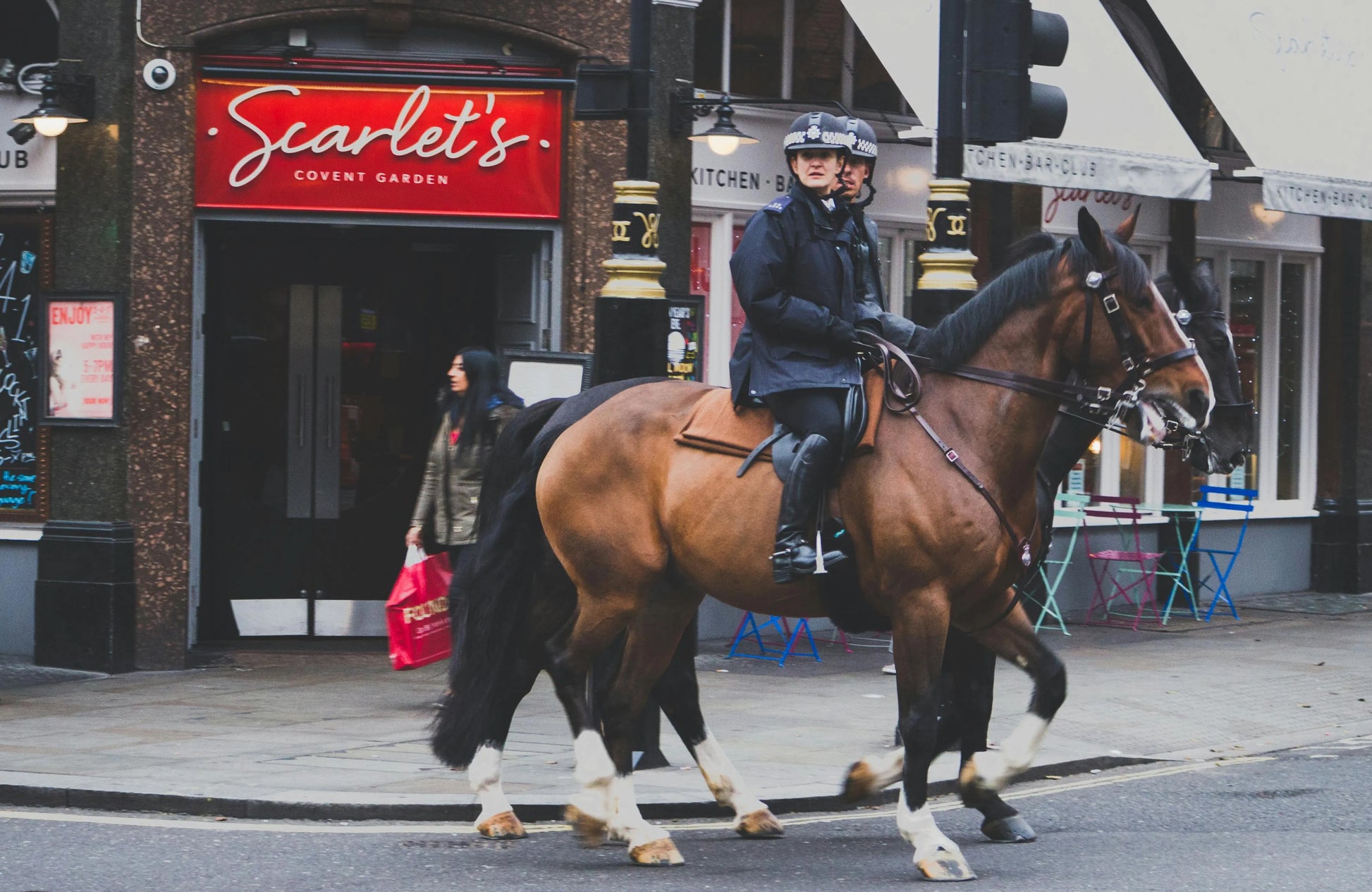 Person riding a horse on a city street with 'Scarlet's' restaurant in the background