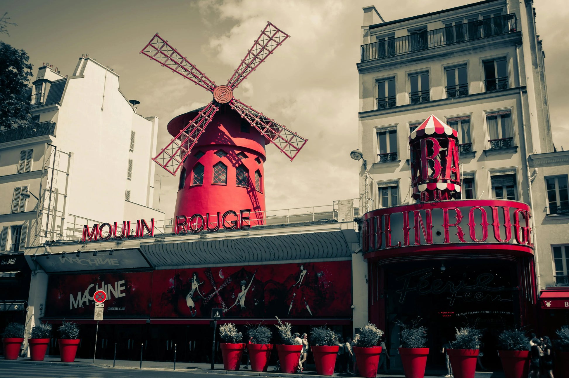 Red windmill structure with 'Moulin Rouge' sign against a gray sky.
