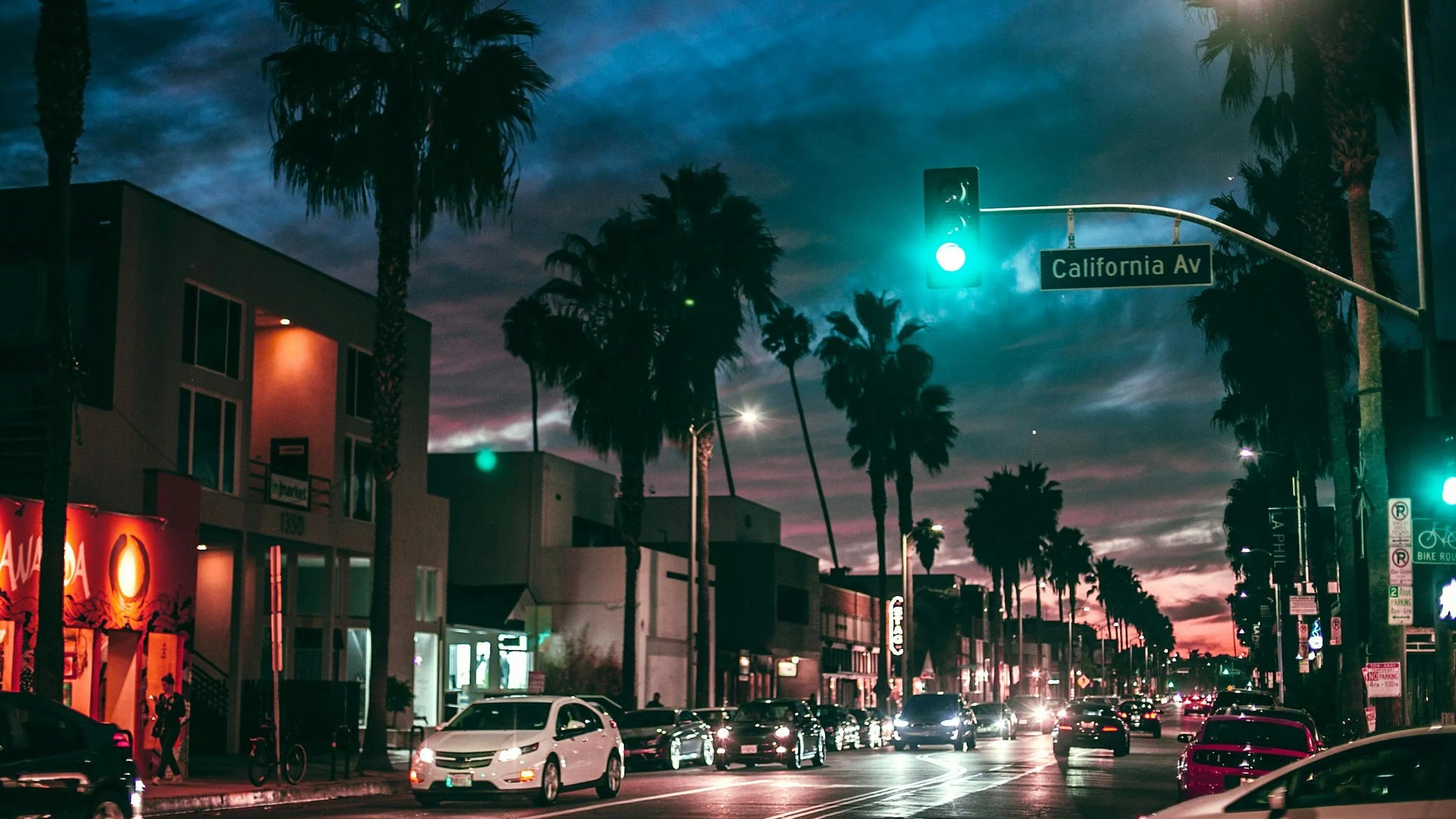 City street at night with palm trees, traffic lights, and buildings.