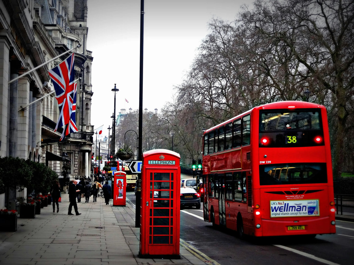 Red double-decker bus and phone booth on a city street with British flags.
