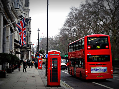 Red double-decker bus and phone booth on a city street with British flags.