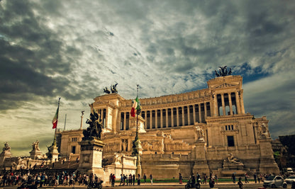 Large historical building with statues and flags under a cloudy sky