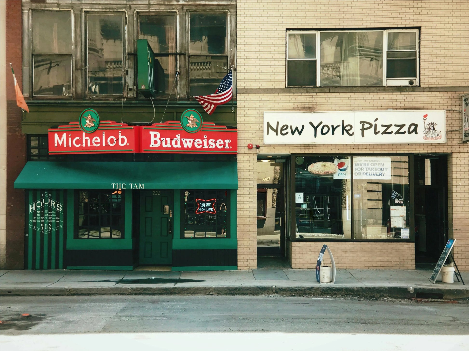 Two storefronts on a city street, one with a green awning and the other with a red and white sign.
