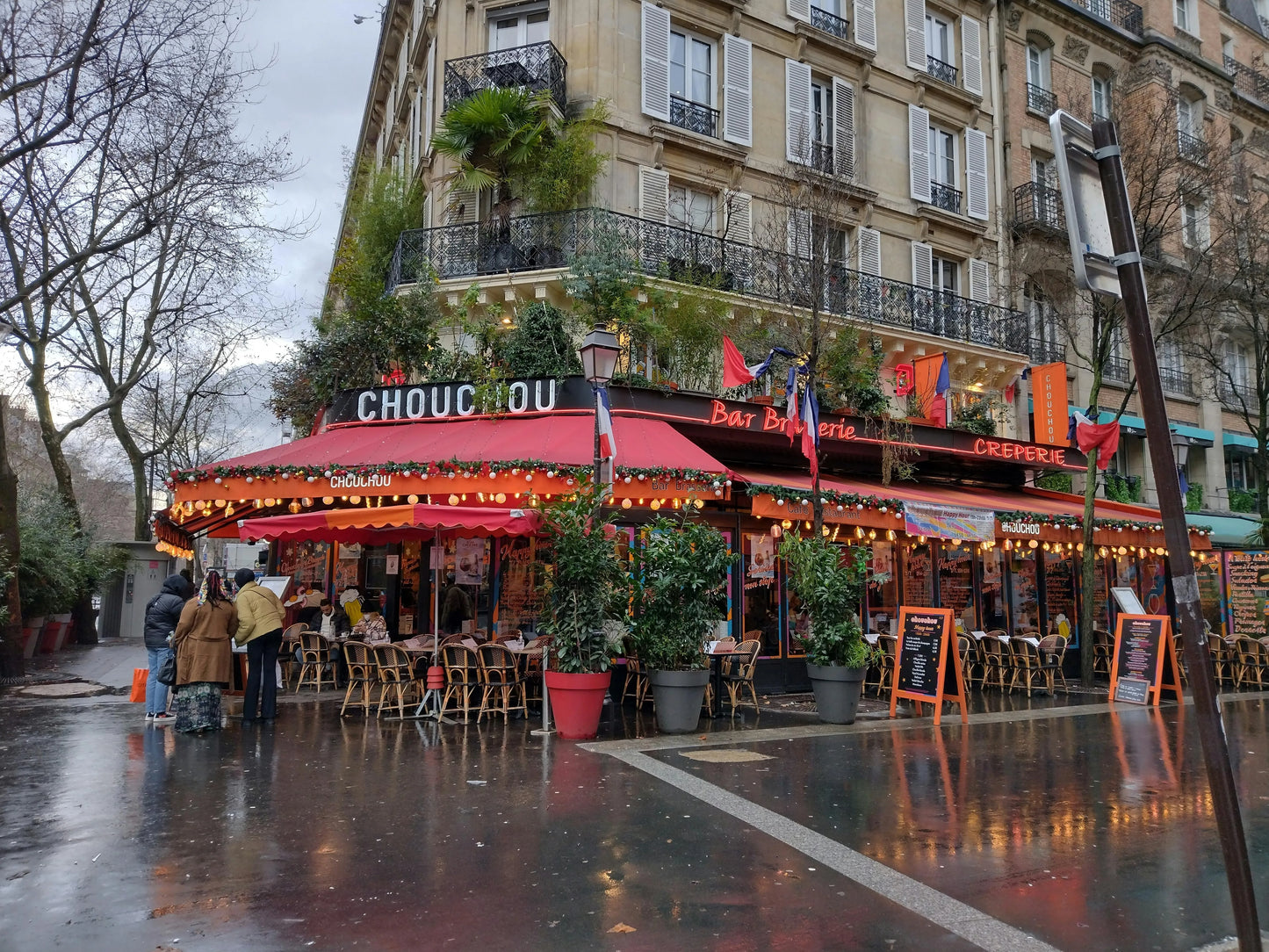 Outdoor cafe with red awning and 'Chou-Chou' sign in a city street.